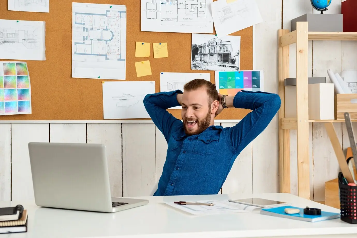 A young, successful businessman celebrating while seated at the workplace with a laptop.